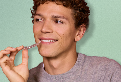 Man holding a clear aligner against a light green background