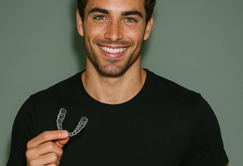 Man holding a clear dental aligner against a plain background