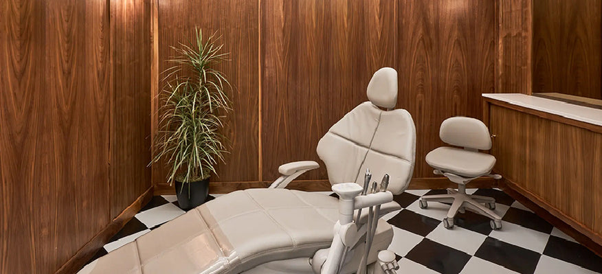 Dental office chair and examination table in a room with wooden walls and checkered floor.
