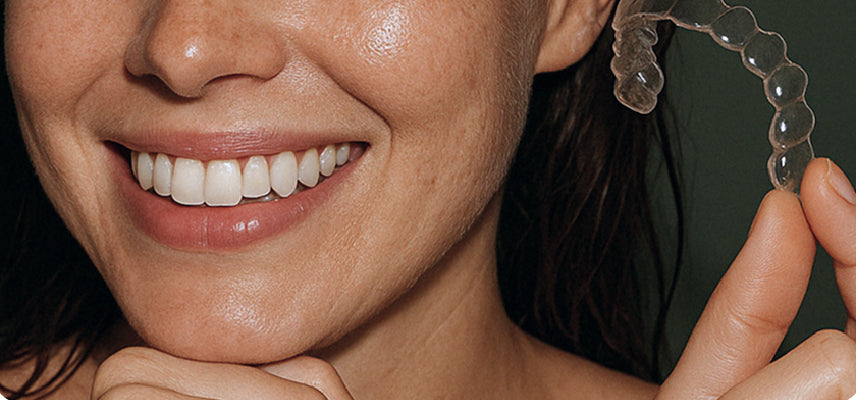Person holding a clear dental aligner with a close-up of their smile.